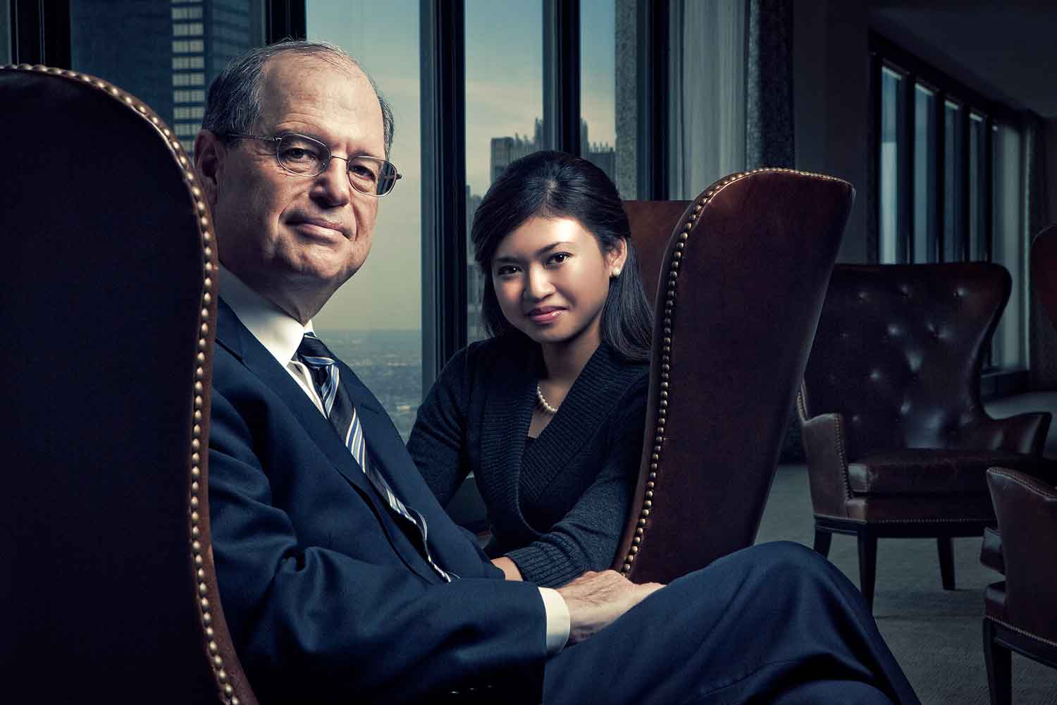 Image of older male and younger female DePaul alumni seated in chairs in office hi rise.