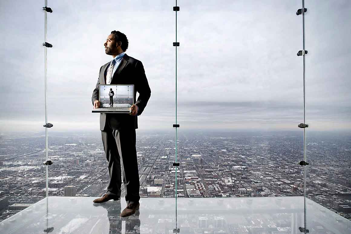 Image of man standing in see through elevator located in Chicago golding a laptop