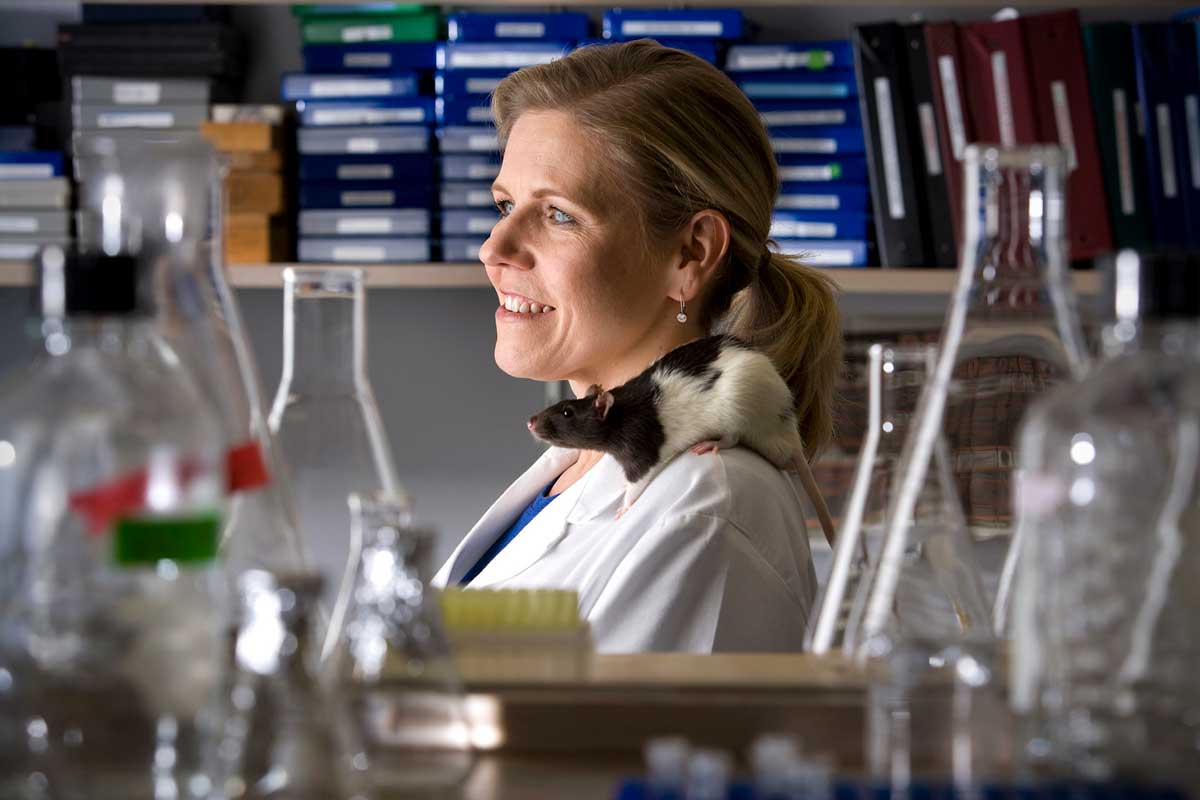 Image of researcher in lab coat surrounded by flasks, beakers, test tubes, and a curious mouse on their shoulders